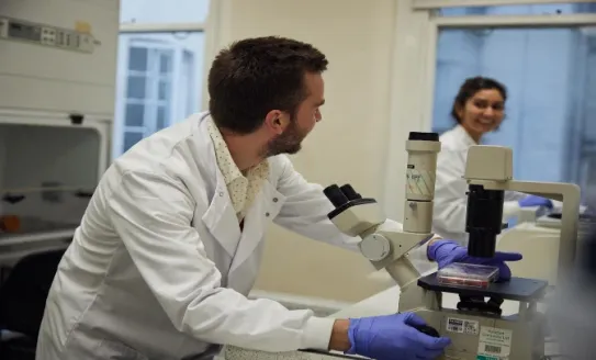 Researcher on microscope smiling at another
