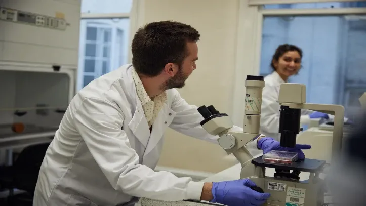 Researcher on microscope smiling at another
