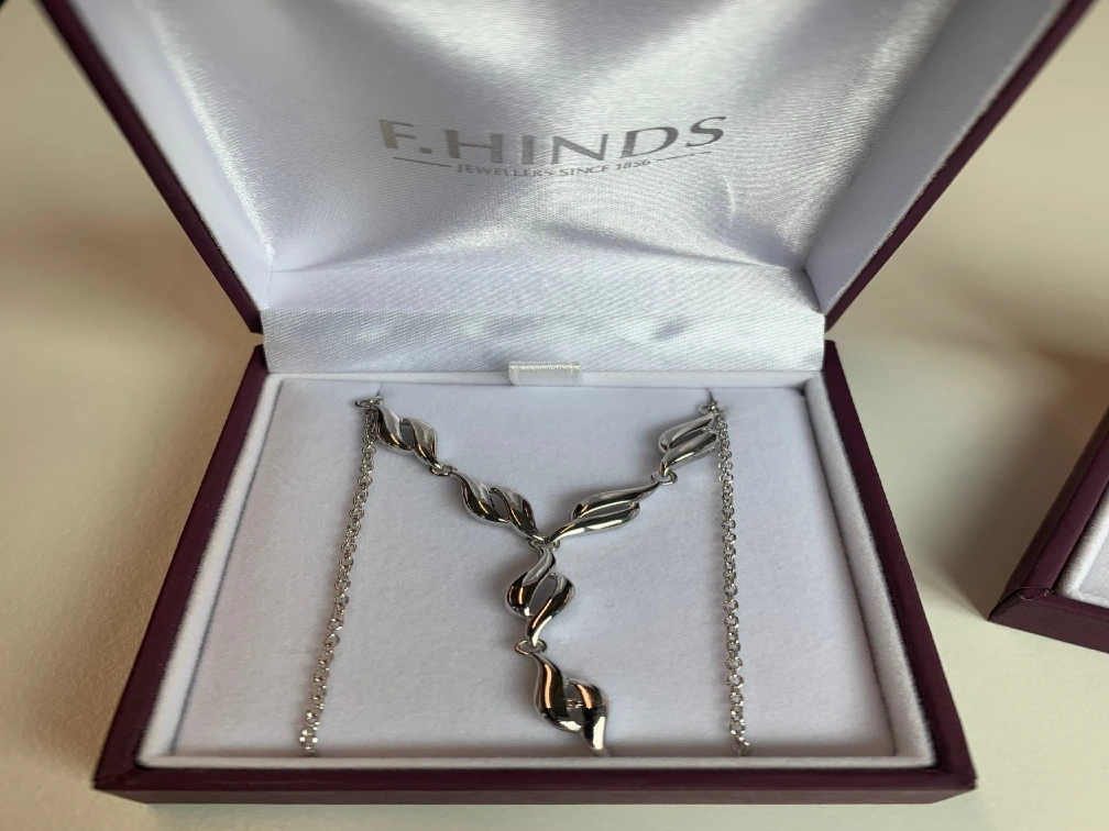A red F.Hinds jewellery box holds a silver necklace.
