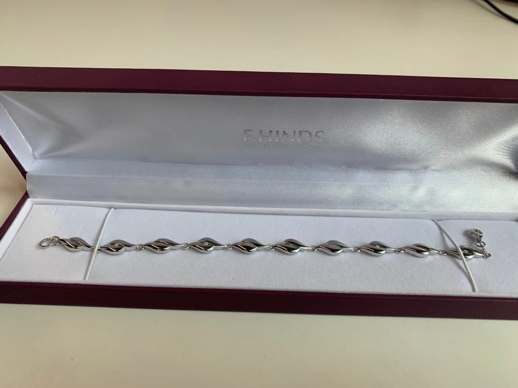 A red F.Hinds jewellery box holds a silver bracelet.