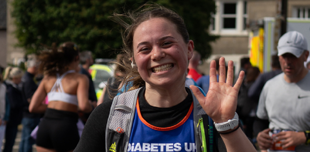 Female wearing Diabetes UK Vest and pack waving at the camera whilst running.
