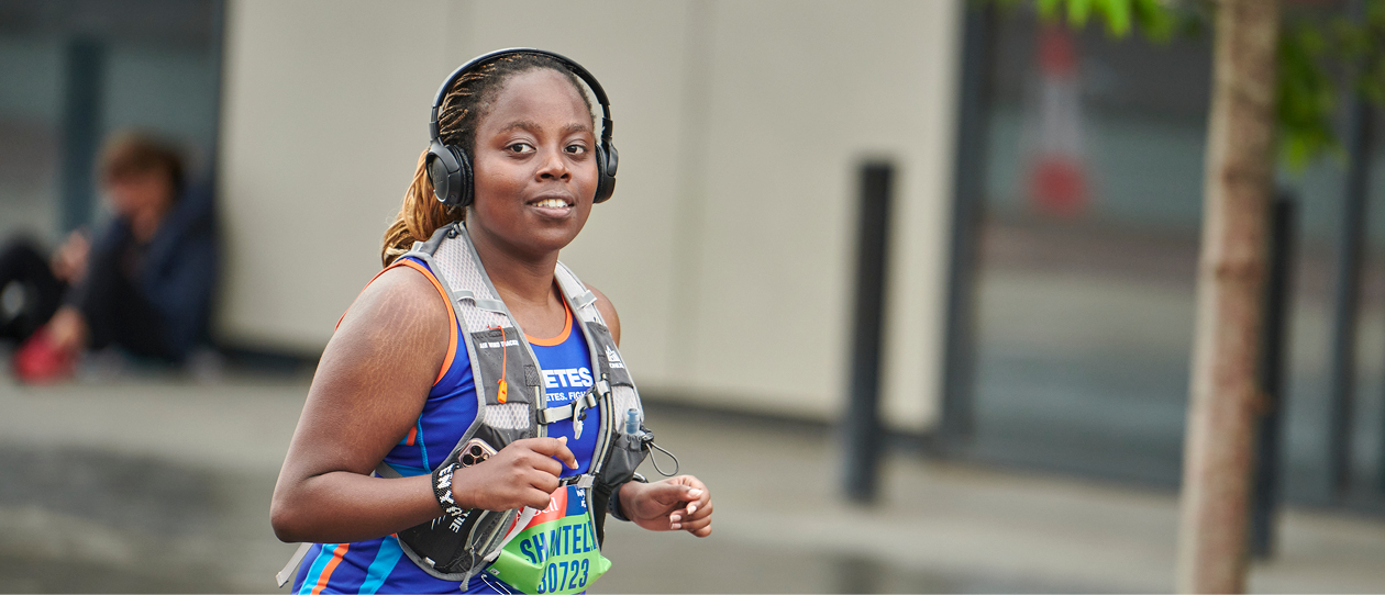 Female runner smiling at camera with over ear headphones and Diabetes UK vest.
