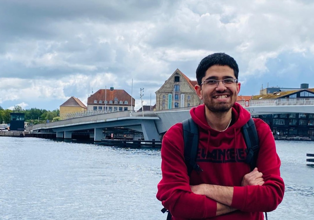 Volunteer Muhammad Qureshi pictured wearing a red hoodie, standing by a river. 