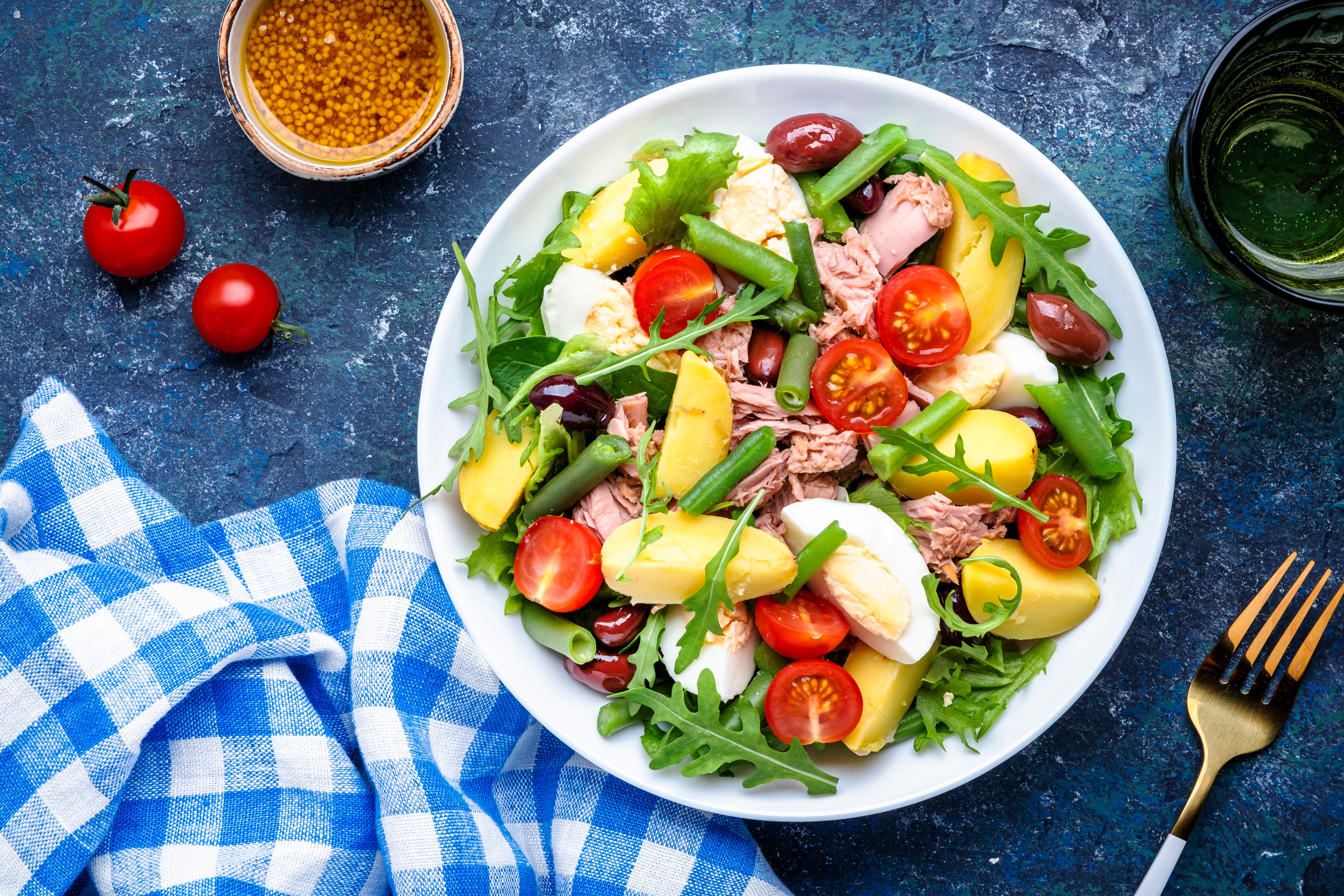 A bowl of nicoise salad on a blue gingham cloth