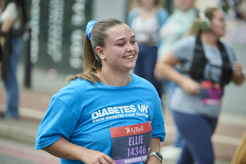 A lady wearing a blue Diabetes UK t-shirt smiles as she's running in the Great Manchester Run.