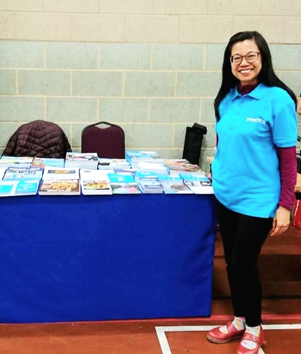 A lady with dark hear and wearing glasses pictured beside a Diabetes UK information table that has several leaflets on it.