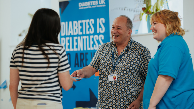 Three people at Diabetes UK event, smiling at handing out a leaflet.
