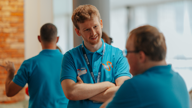 In this photo, a Diabetes UK staff member can be seen talking to a Diabetes UK Young Leader from Together Type 1. The person in focus is wearing a pale blue Diabetes UK Together Type 1 polo shirt, with a blue Diabetes UK lanyard around his neck.
