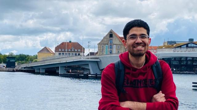 Volunteer Muhammad Qureshi pictured wearing a red hoodie, standing by a river. 