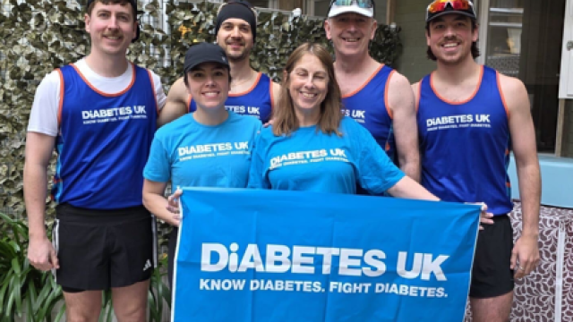 Five participants wearing Diabetes UK running tops pose together holding a Diabetes UK banner before a marathon event.