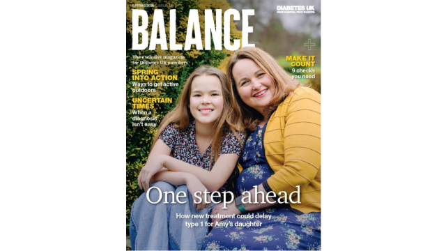 A lady wearing a yellow cardigan and blue dress sits next to her daughter, a young girl wearing a floral top and blue jeans. They're smiling at the camera while sitting in front of a bush with yellow flowers. 