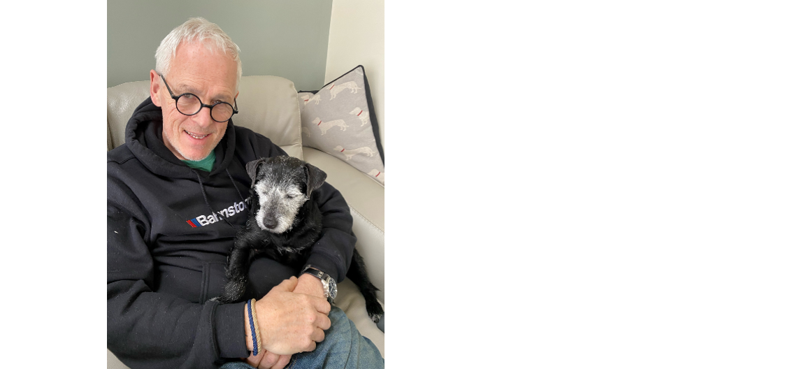 Andy sits on a sofa smiling at the camera with his dog on his lap.