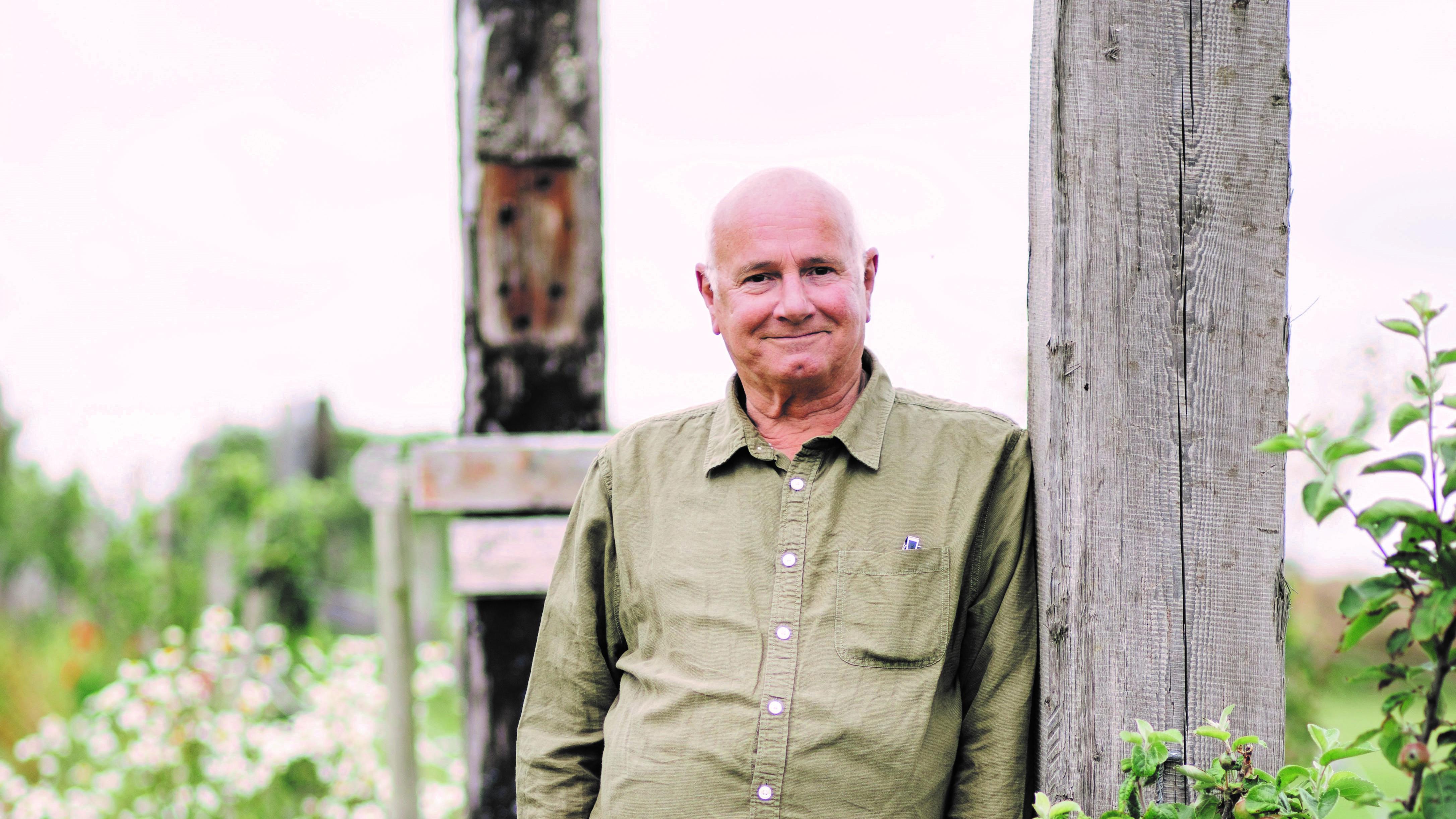 A man wearing a green shirt, smiling and leaning against a wooden post