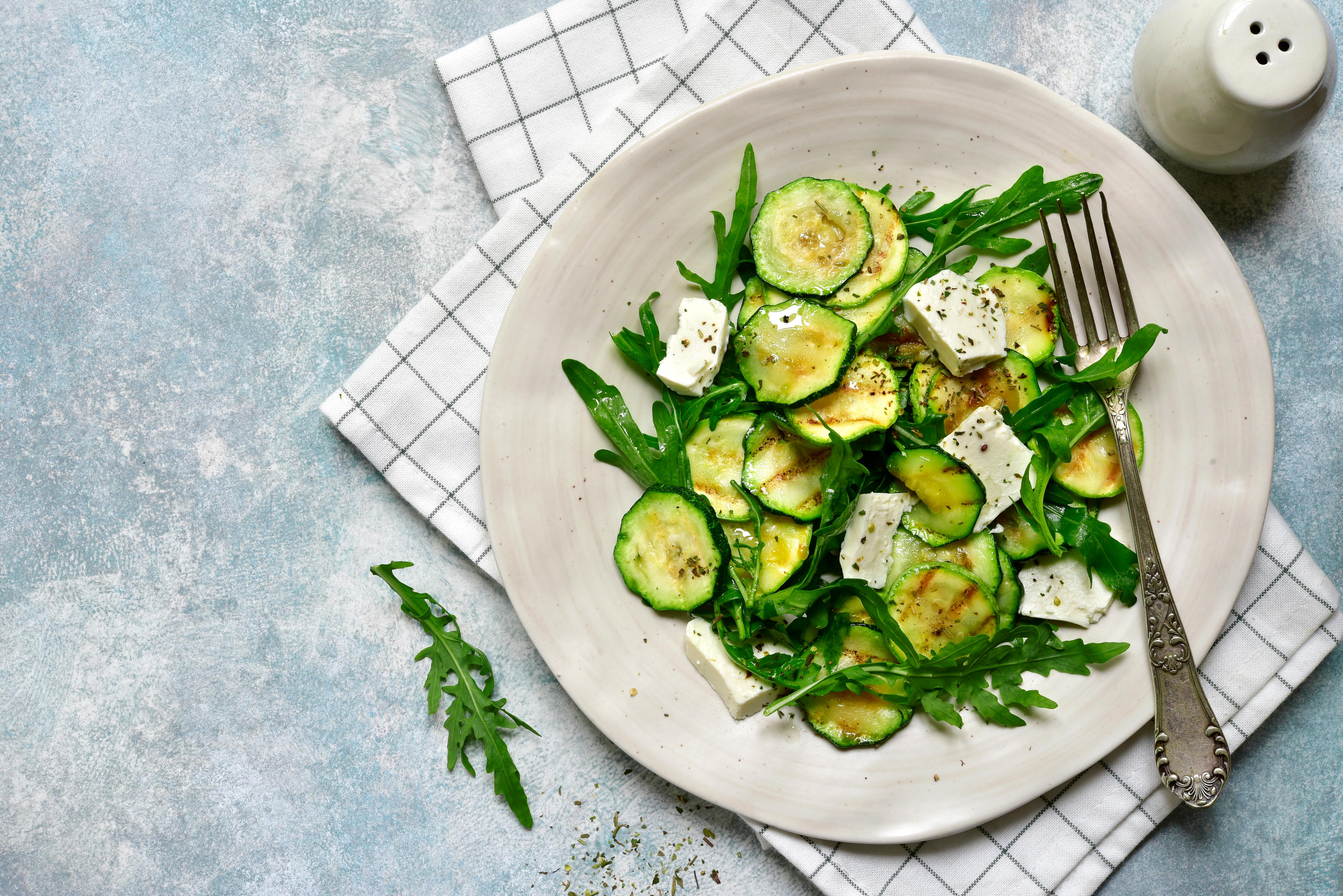 Plate with bright green sliced courgette and white feta cheese on it.