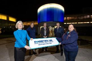 5 people holding a Diabetes UK poster in front of Coleraine Council building lit up blue for World Diabetes Day