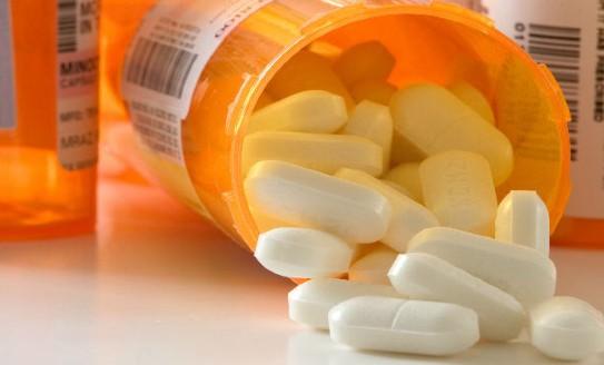 An orange pill bottle on its side with white pills coming out of it