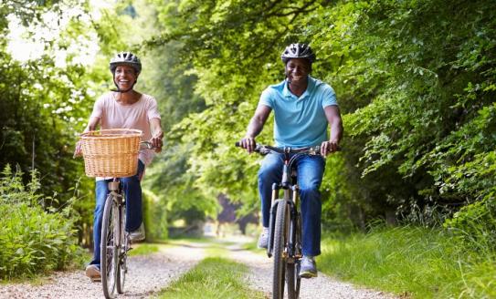 Woman and man on bikes, smiling, on a tree-lined path