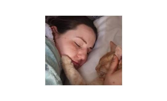 A photo of Lili snoozing in bed with her ginger cat next to her