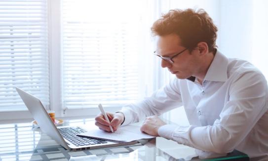 man writing paper laptop