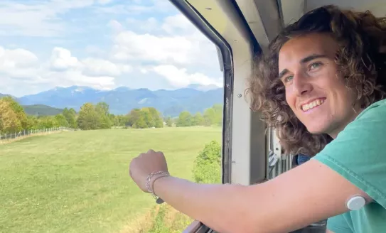 A young man looks out of a train window onto a field