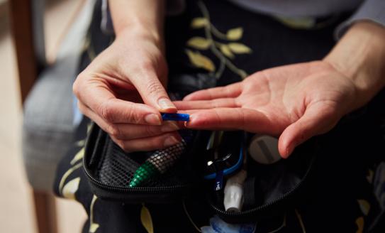 In this image, it is focused on a person's hands. They are pricking their finger to test their blood, in order to monitor their diabetes affected blood sugar levels.