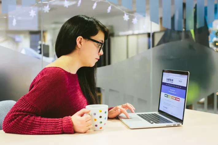 A woman holding a mug and looking at the Diabetes UK website on a laptop