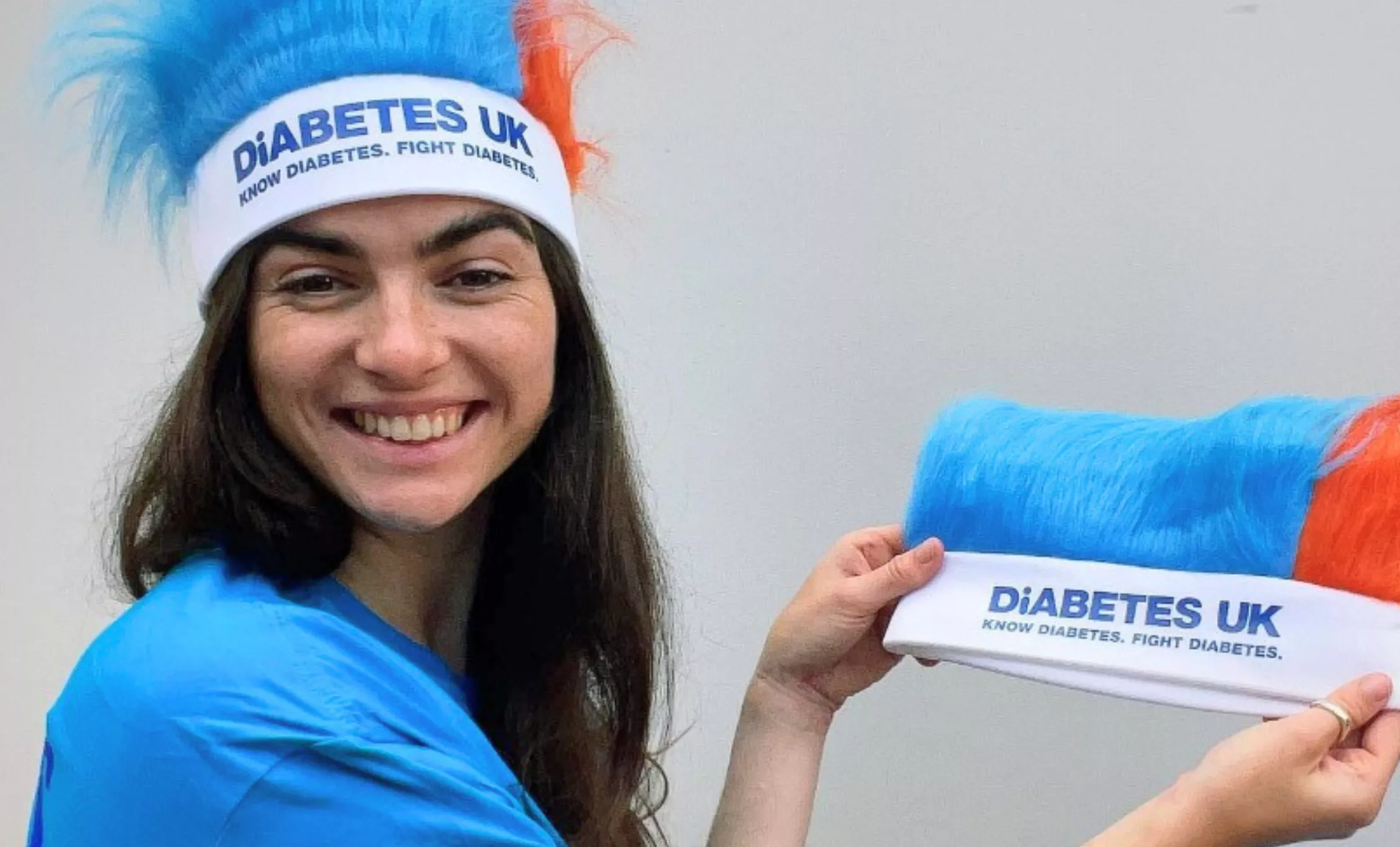 Megan with Diabetes UK blue and orange hat on, holding up another hat.