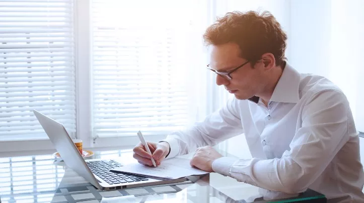 man writing paper laptop