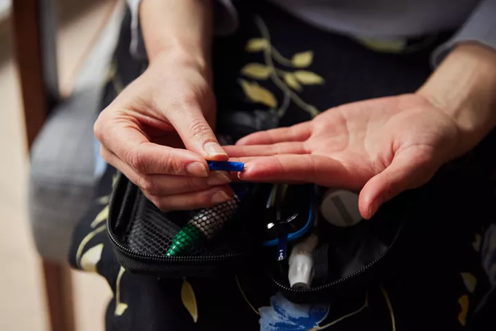 In this image, it is focused on a person's hands. They are pricking their finger to test their blood, in order to monitor their diabetes affected blood sugar levels.