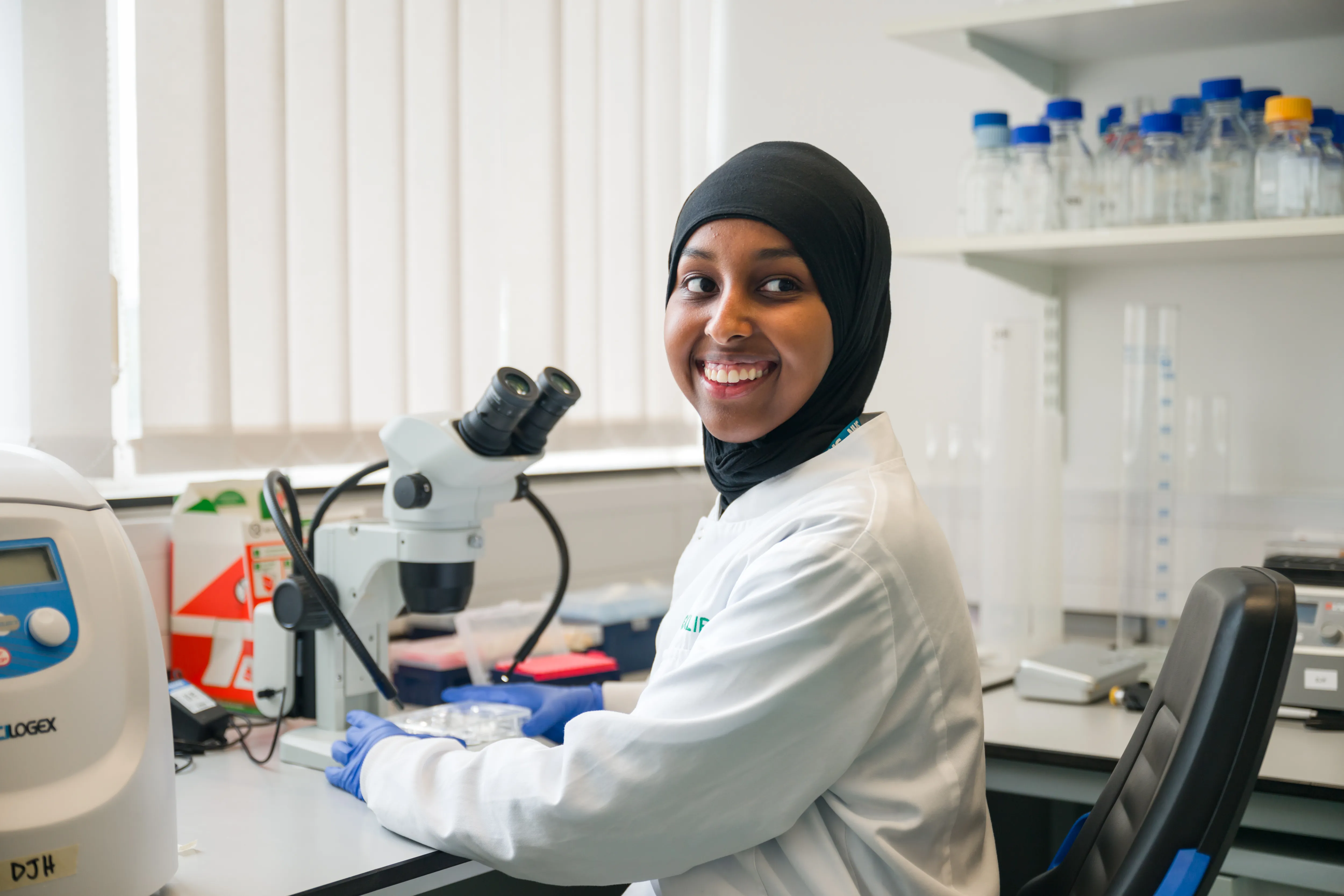A Black researcher sitting next to a microscope in the lab, smiling