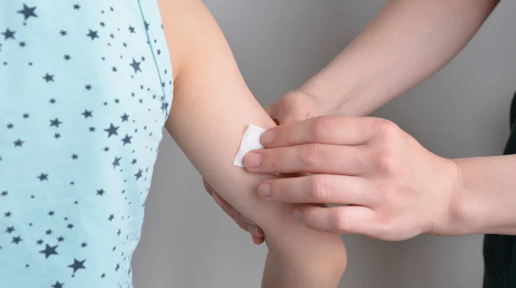 Person using non-alcohol cleansing wipe on back on child's arm