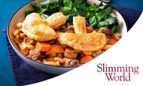 A white bowl with steak, mushrooms, carrots, and beans, puff pastry, and greens