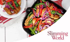 A mixture of chicken, green and red peppers, and red onion slices in a skillet on a white table. Next to the skillet is a white plate on a red and white striped tea towel with a portion of the mixture and sliced tomatoes