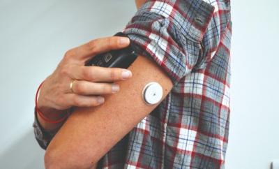 A person in a grey and red shirt scanning their Flash monitor on the back of their arm